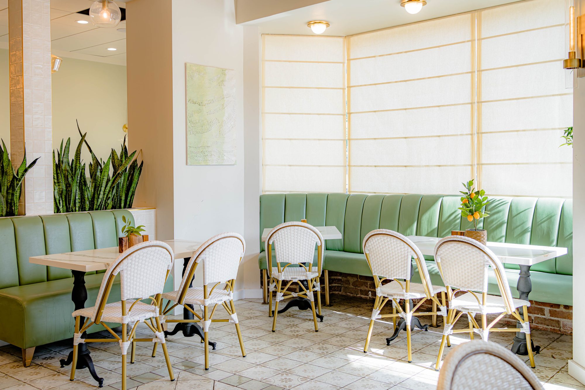 Lamalo café interior with sage green banquettes, cane bistro chairs and brass pendants