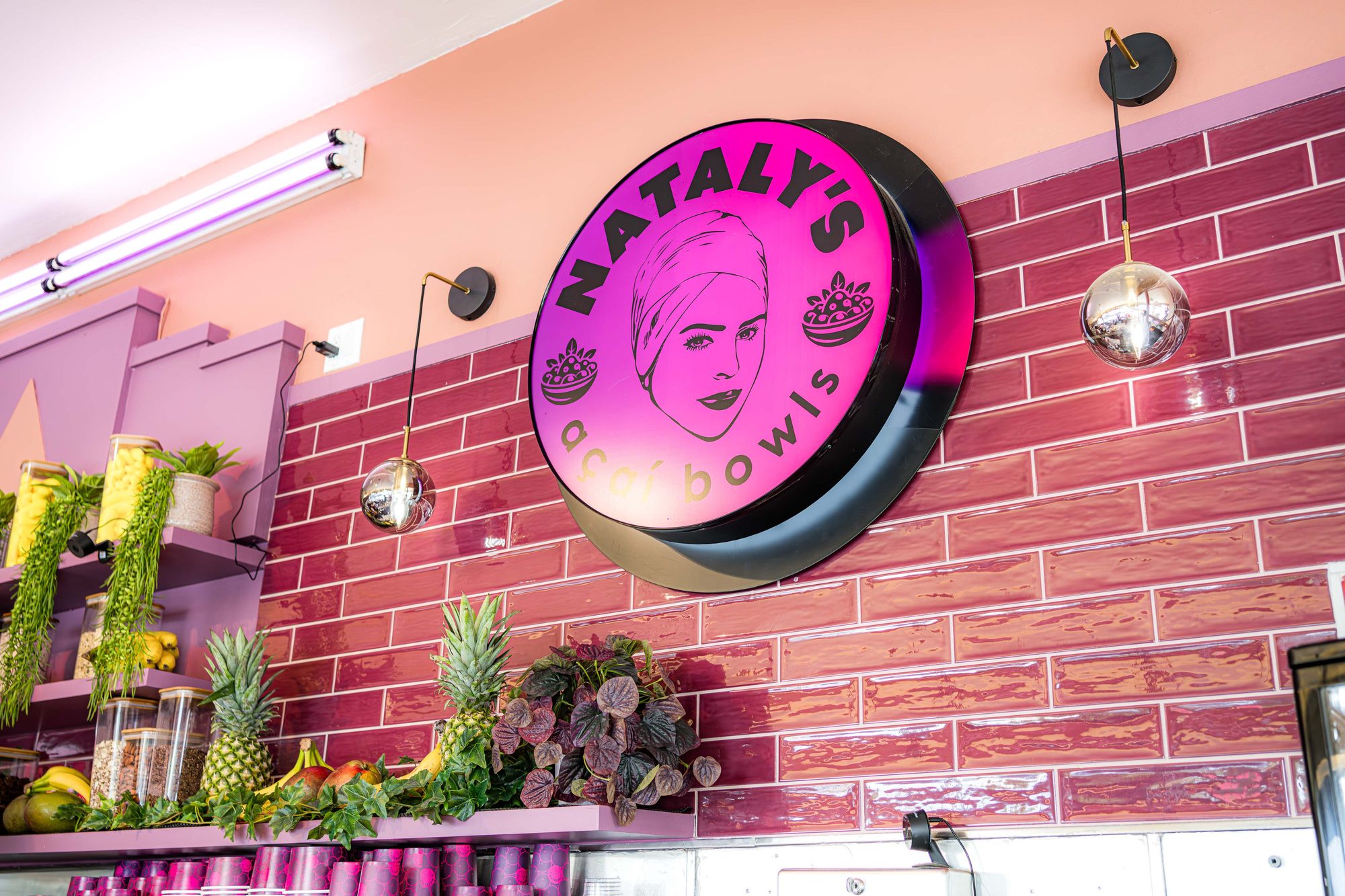 Neon Nataly's Acai logo mounted on the magenta brick wall